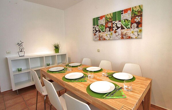 A dining area with a wooden table set for four, white chairs, and a green table runner. - 2 bedroom beautiful apartment in Ribarica (Ribarica)