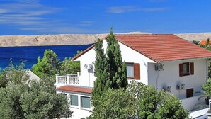 Un edificio blanco con techo rojo, rodeado de vegetación, con vista a un cuerpo de agua y un paisaje montañoso.