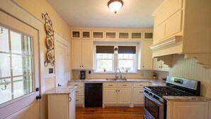 A kitchen with white cabinets, a dishwasher, a stove, and a window with blinds.