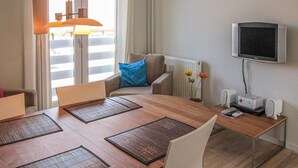 A modern living room with a wooden dining table, a sofa with a blue pillow, a television mounted on the wall, and a radiator.