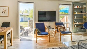 A spacious living room with a large TV, two blue armchairs, a wooden coffee table, and a glass coffee table.