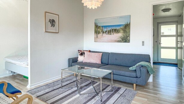 A living room with a sofa, a glass coffee table, a framed picture, and a painting on the wall.