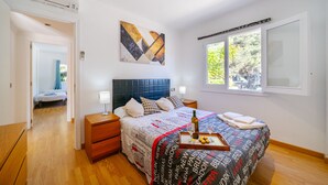 Un dormitorio con una cama, mesitas de noche, una ventana y un cuadro en la pared.