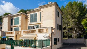 Un edificio de dos pisos con fachada color beige, contraventanas verdes y un balcón con barandilla.