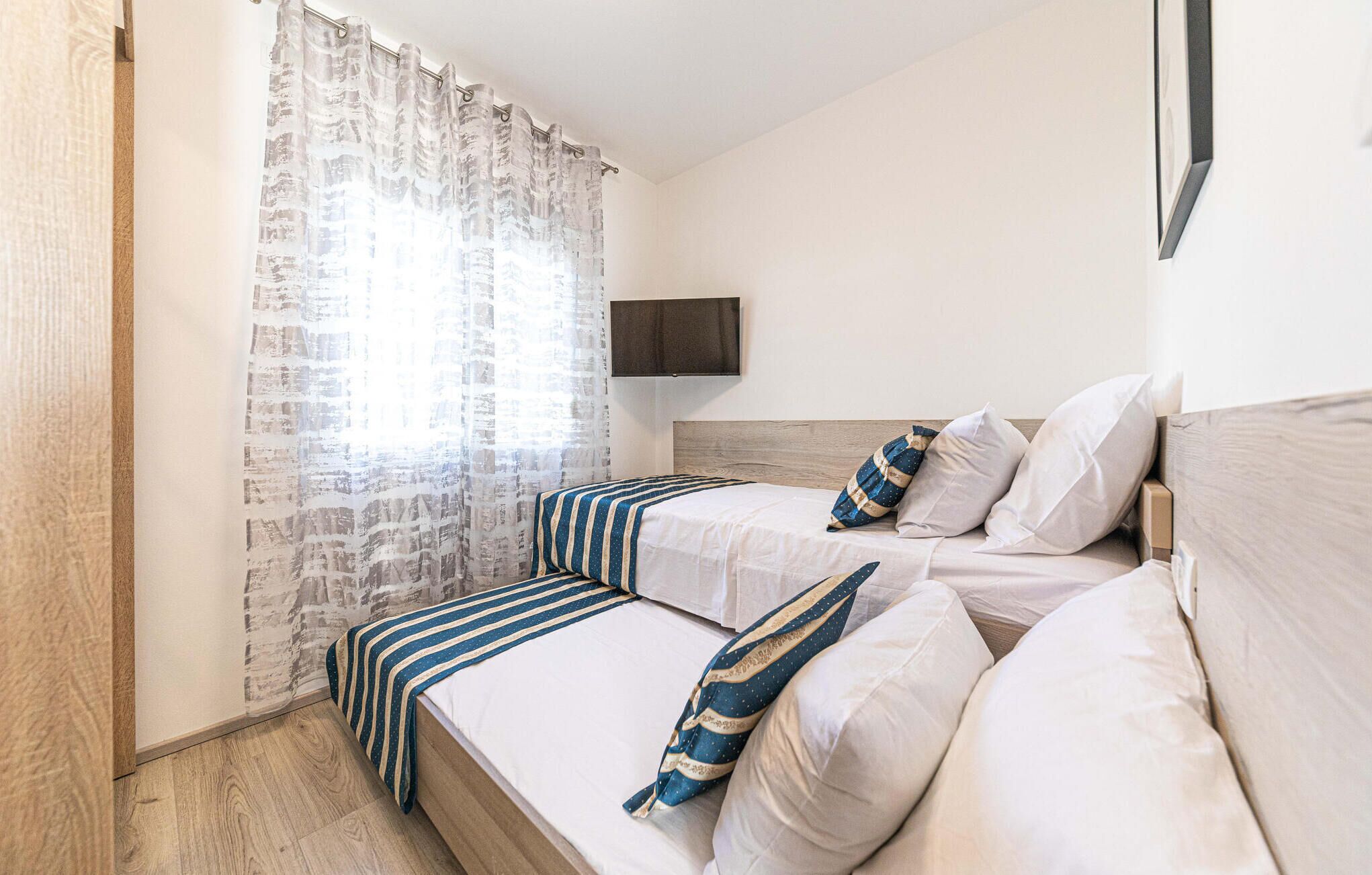 A bedroom with two beds, a TV mounted on the wall, and a window with curtains.