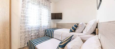 A bedroom with two beds, a TV mounted on the wall, and a window with curtains.