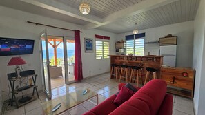 Ein Wohnzimmer mit einem roten Sofa, einem Glastisch, einem Fernseher und einer Küchenzeile mit einer Bar.