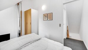Une chambre à coucher au style minimaliste, avec un lit, une armoire et un tableau accroché au mur.
