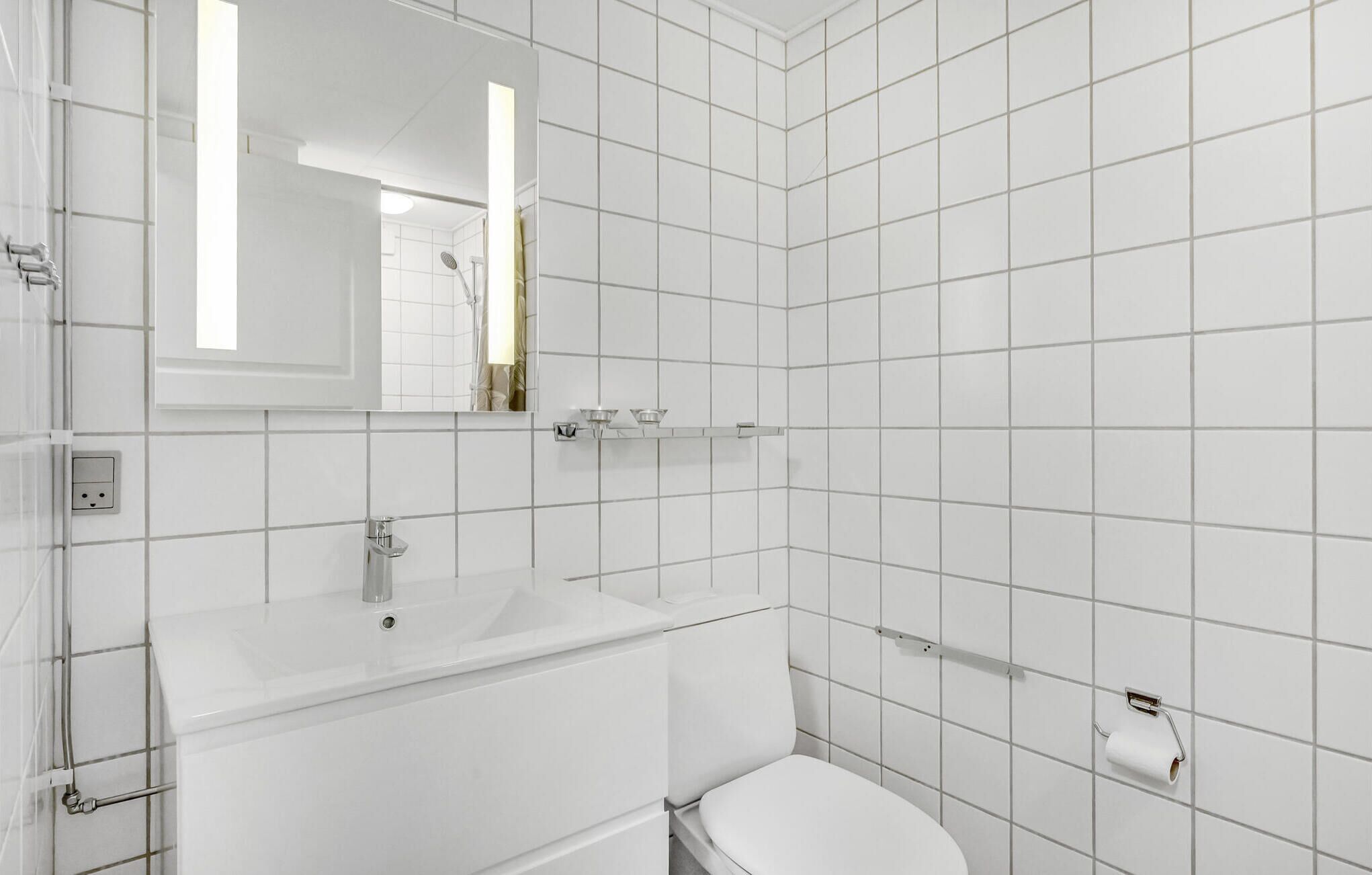 A bathroom with white tiles, a sink, a toilet, and a mirror.