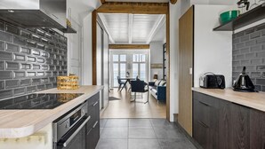 Une cuisine moderne avec un mur de fond en briques, des poutres en bois au plafond et une vue sur l’espace repas.