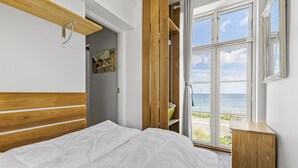 Une chambre à coucher avec un lit, une tête de lit en bois, une vue sur la mer par une grande fenêtre et un tableau accroché au mur.