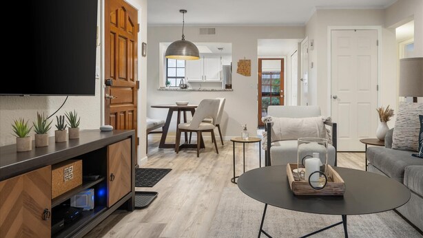 A modern living room with a flat-screen TV, a coffee table with decorative items, a sofa, and a dining area with a table and chairs. - Sonoran Style 2BR/2BA w. Free Parking & Pool (Scottsdale)