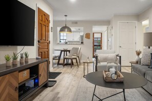 Ein modernes Wohnzimmer mit Flachbildfernseher, Couchtisch mit Dekoration, Sofa und Essbereich mit Tisch und Stühlen.