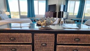 A hotel room with a bed, a TV, a desk with a computer, wicker baskets, and a view of the city. - Tootsie's Next Door! Top of The Gulf! (Panama City Beach)