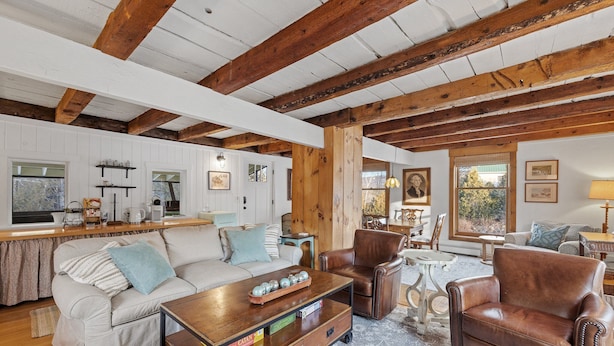 A spacious living room with a wooden ceiling, a sofa, a coffee table, and a leather armchair.
