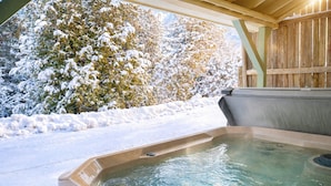 A hot tub in a covered outdoor area with snow-covered trees and a wooden fence in the background.