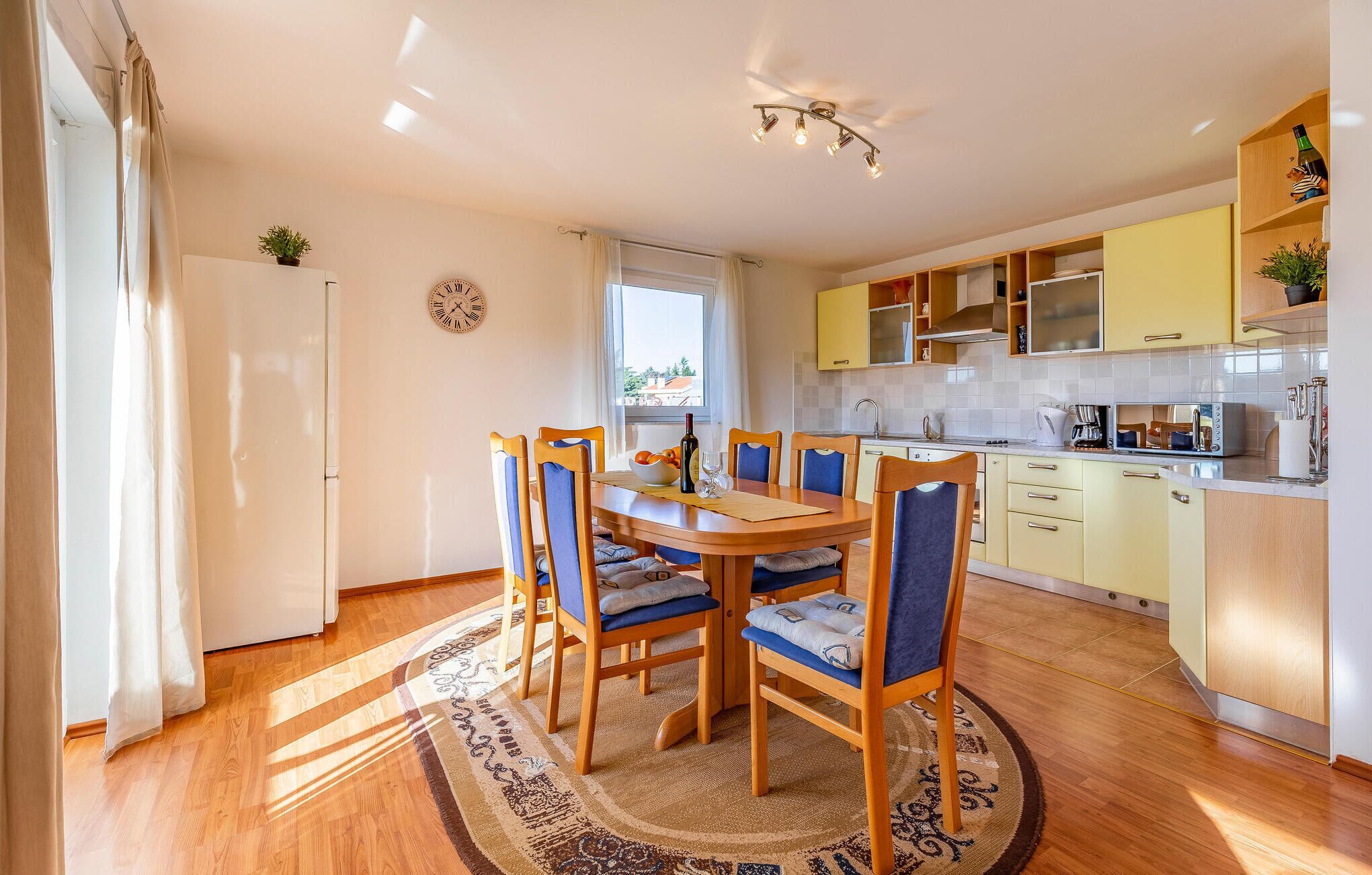 A modern kitchen with wooden cabinets, a dining table with chairs, and a large window.