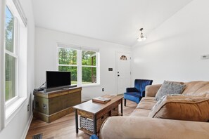Una habitación con una mesa de centro de madera, un sofá, un televisor sobre un mueble de madera y una puerta con ventanal.