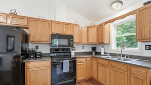 Una cocina moderna con armarios de madera, un refrigerador negro, un microondas y una estufa.