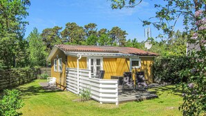 A yellow cabin with a fenced patio area, surrounded by greenery and trees.