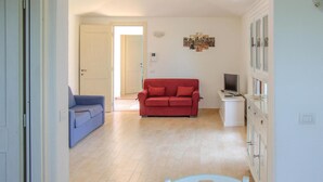 Una sala de estar con un sofá rojo, un sillón azul, un armario blanco y un televisor.