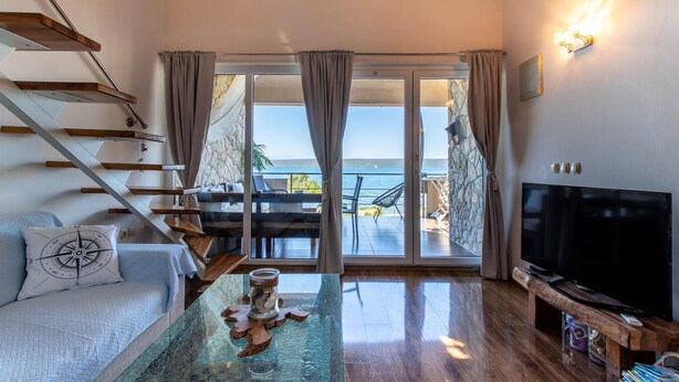 A modern living room with a TV, a glass coffee table, and a view of the sea through large sliding doors. - 2 bedroom gorgeous apartment in Dobropoljana (Dobropoljana)