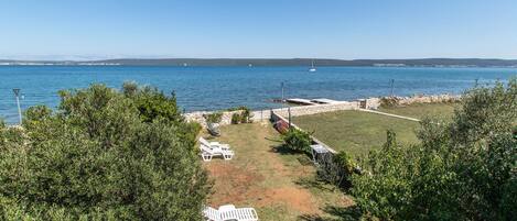 A coastal property with a grassy area, white lounge chairs, and a stone wall overlooking the sea.
