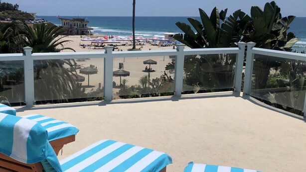 A balcony with two striped lounge chairs, a palm tree, and a beach view. - Oceanfront 4 bedroom villa w/ 2 masters and views (Encinitas)