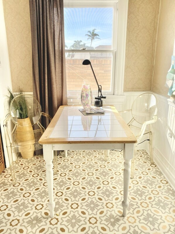 Een hoekzaal met een tafel, stoel, lamp en raam met uitzicht op palmbomen.