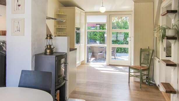 Una cucina con piano cottura, tavolo da pranzo, sedie e vista sul giardino tramite porte vetrate.