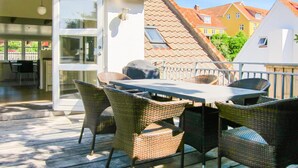 Una veranda esterna con mobili in vimini, un tavolo e una porta vetrata che dà su un ambiente interno.