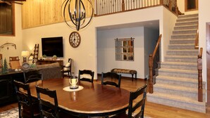 Un comedor con mesa y sillas de madera, un candelabro y una escalera que sube a un nivel superior.