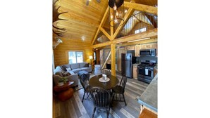 A spacious wooden cabin interior with a dining area, kitchen, and a staircase leading to an upper level. - Beautiful Comfy Alaskan Log Home 1 (Wasilla)
