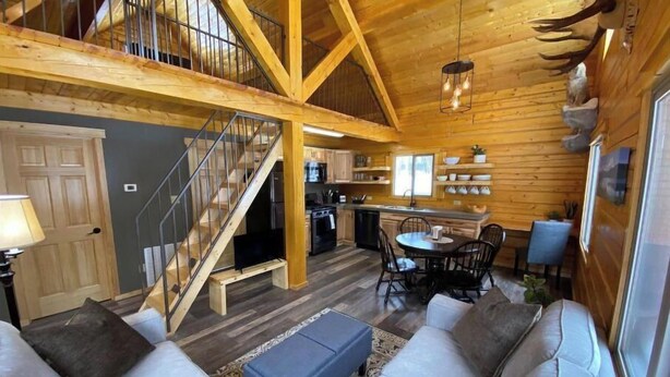 A spacious log cabin interior with a high ceiling, a staircase, a dining area, and a cozy seating area. - Beautiful Comfy Alaskan Log Home 1 (Wasilla)