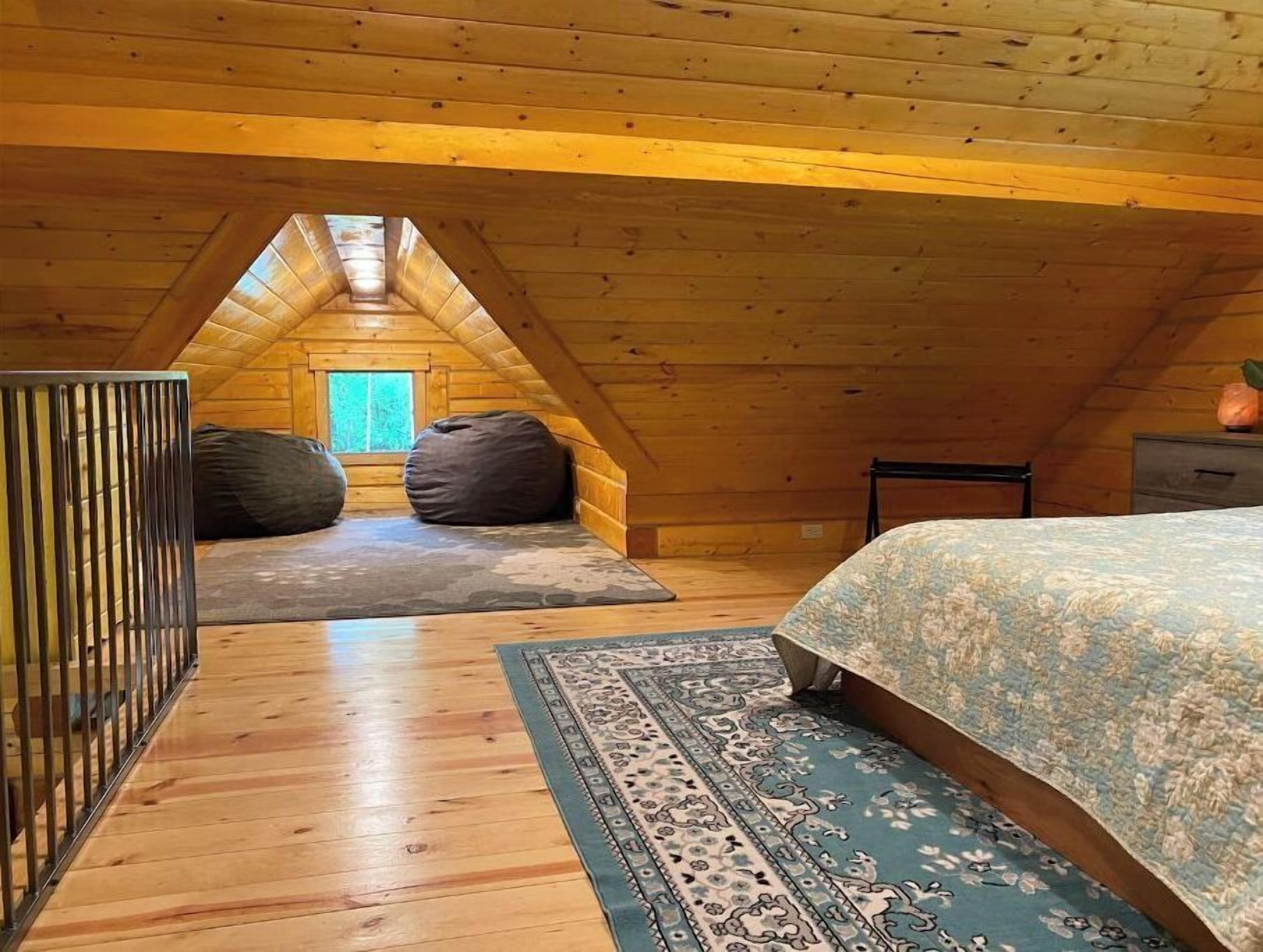 Een gezellig slaapkamer onder het dak, met een schuine plafond, een groot bed, twee relaxfauteuils, een kamerkleed met patroon, en een raam met uitzicht.