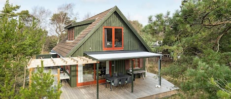En træhytte med terrasse, overdækket terasse og spiseplads.