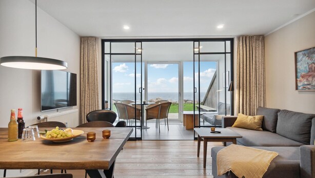 Ein modernes Wohnzimmer mit einem Holzesstisch, einer Couch und einem großen Fenster mit Meerblick.