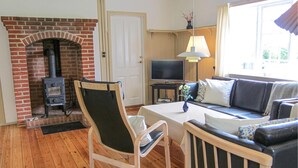 A cozy living room with a brick fireplace, a television, a sofa, and a chair. - Amazing home in Gudhjem with house sea view (Gudhjem)