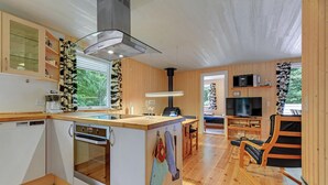 Une cuisine moderne dotée d’un four encastré, d’une plaque de cuisson en verre et d’une hotte en acier inoxydable. On y trouve un coin repas avec une table et des chaises en bois. Un téléviseur est fixé au mur, et une grande fenêtre laisse entrer la lumière naturelle.