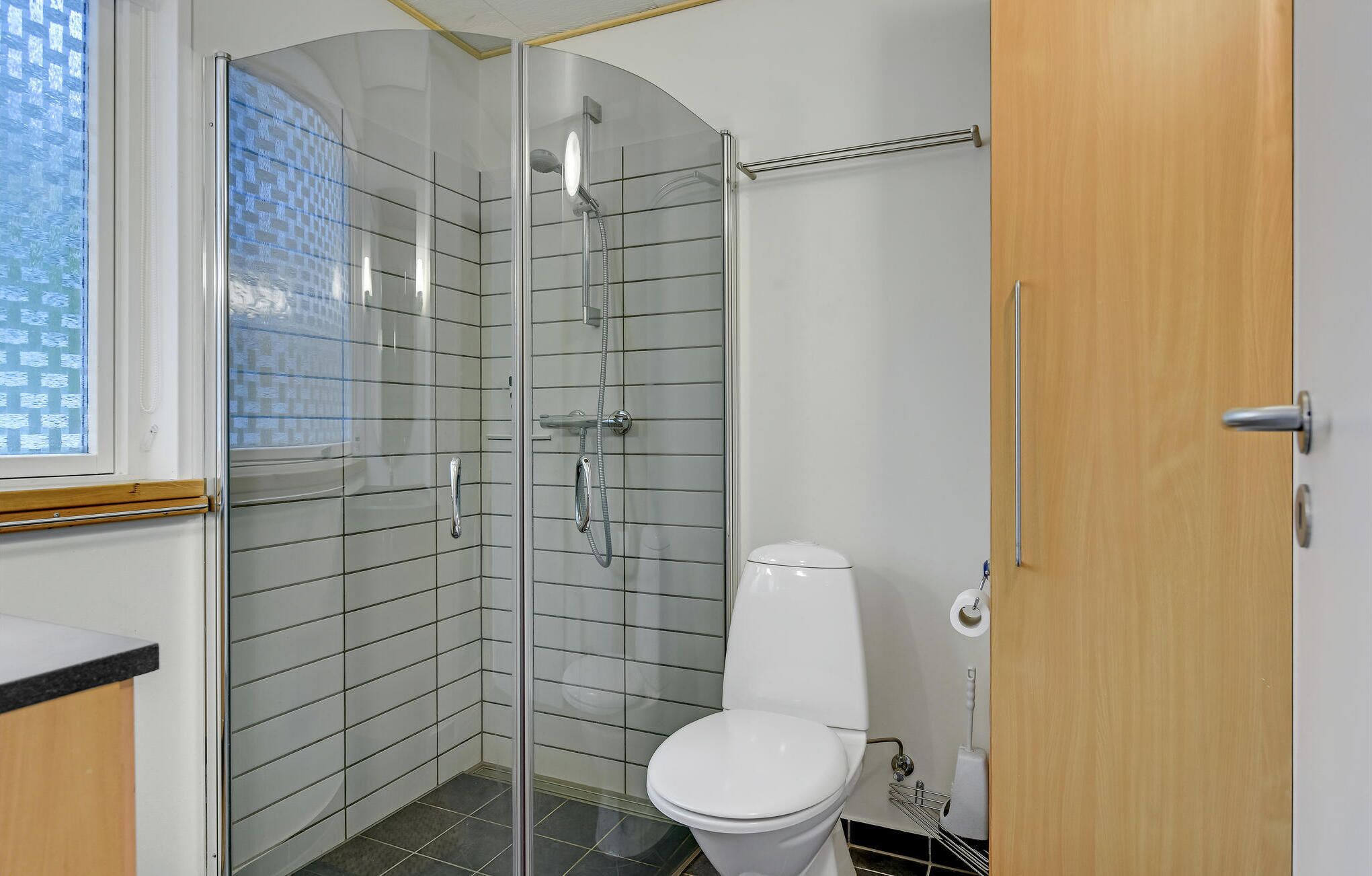 A modern bathroom with a glass-enclosed shower, a white toilet, and a wooden door.