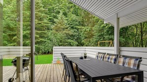 Une terrasse extérieure couverte, avec une table et des chaises en bois, un barbecue et une balançoire.