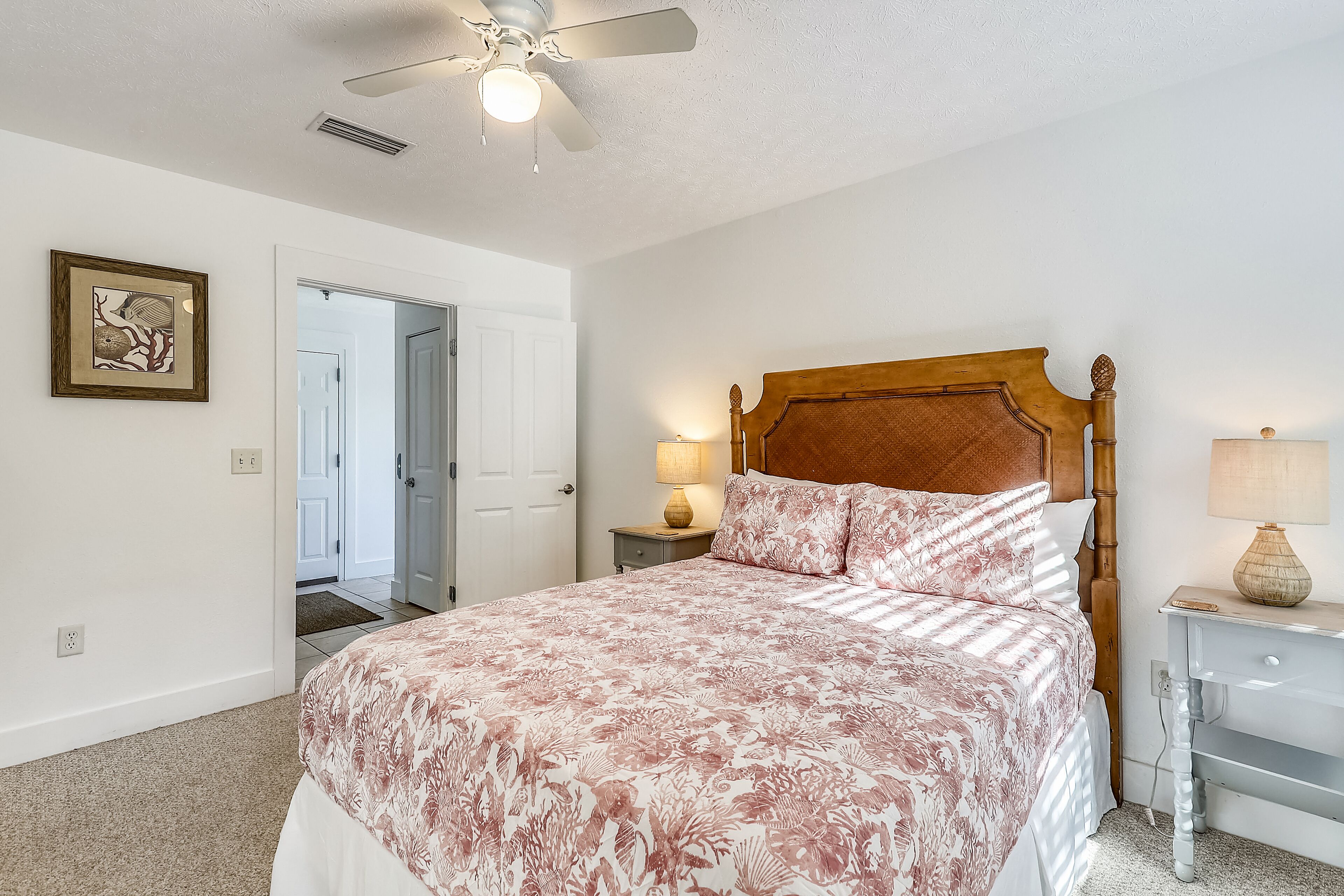 A bedroom with a large bed, a wooden headboard, two bedside lamps, a nightstand, and a ceiling fan.