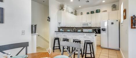 Una cocina moderna con armarios blancos, una isla de mármol y un comedor con mesa y sillas de madera.