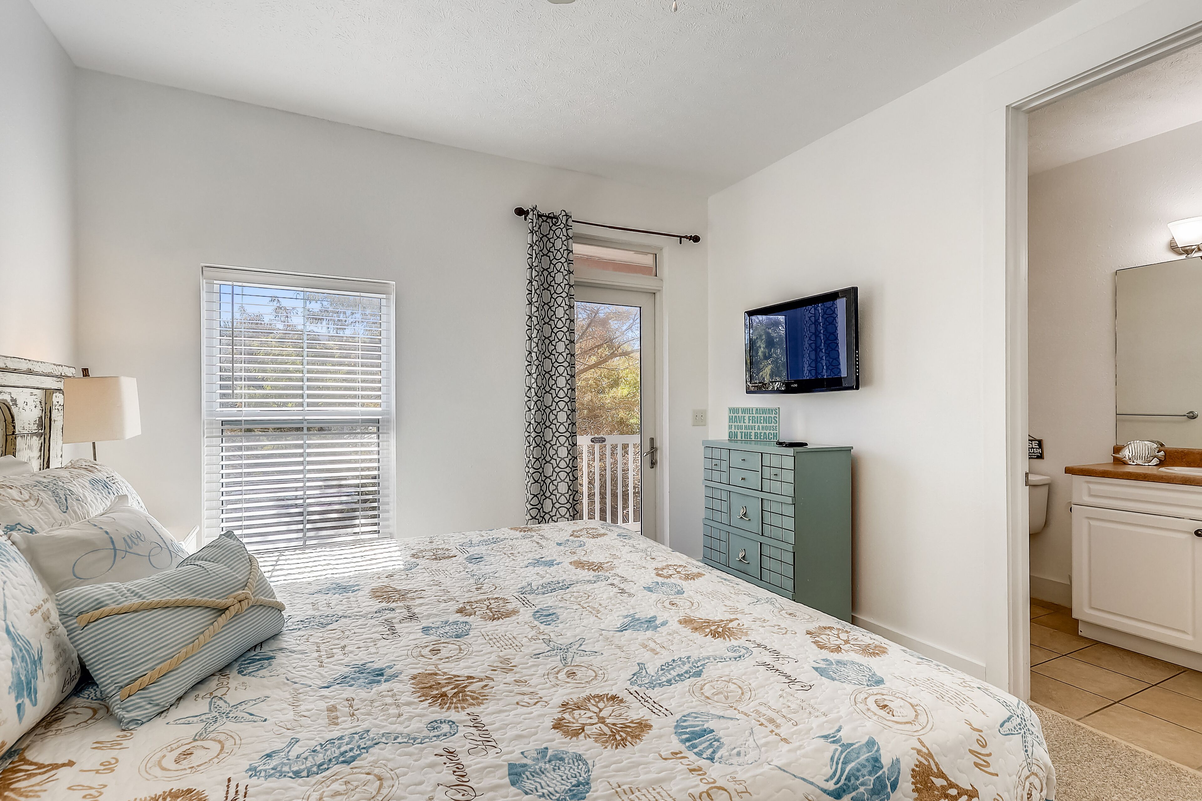 A bedroom with a bed, a dresser, a television, and a window with blinds.