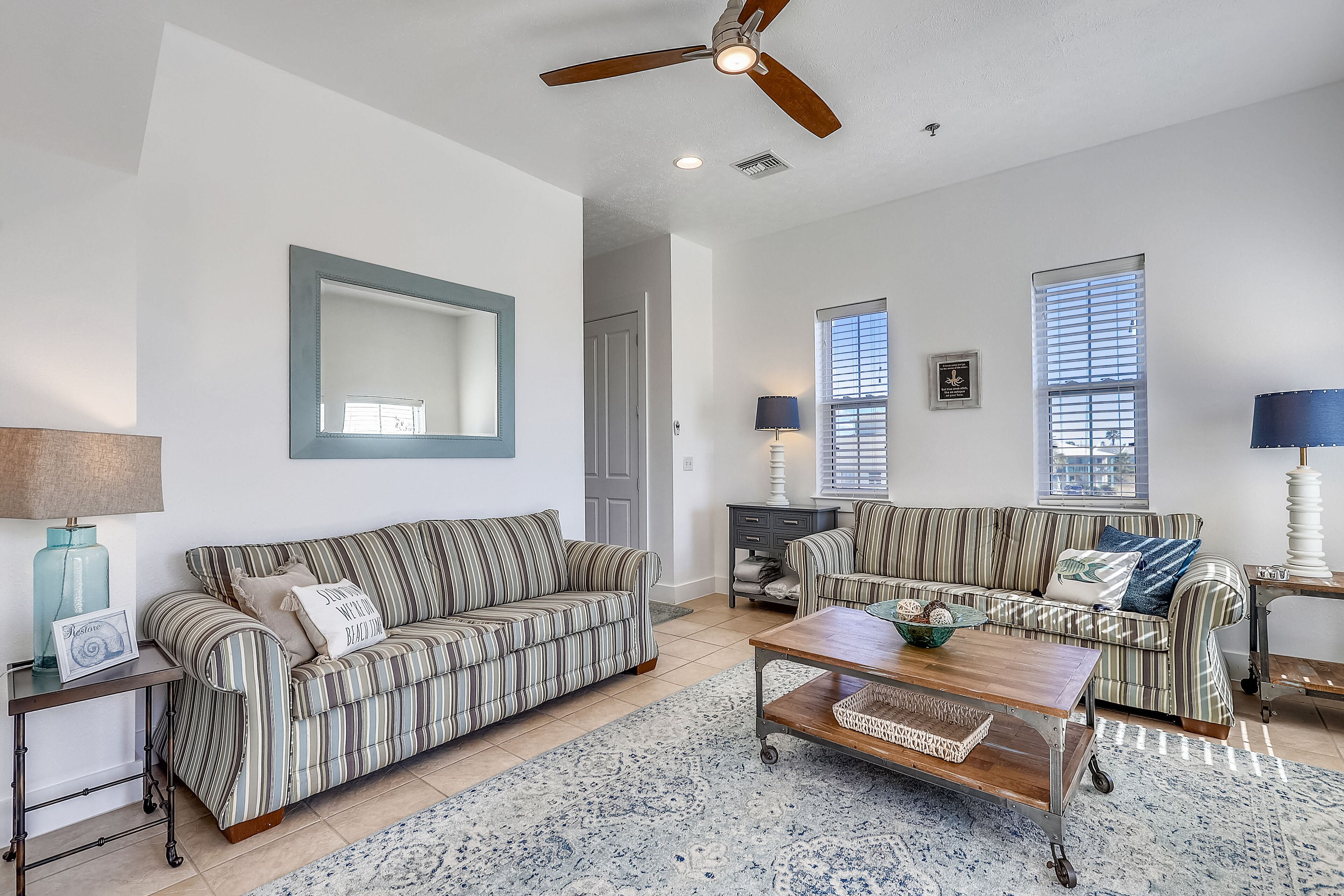 A spacious living room with two striped sofas, a coffee table, and a ceiling fan.