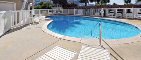 A swimming pool with a white fence, lounge chairs, and a clear blue sky.