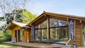 Une cabane en bois dotée de grandes fenêtres, d’une terrasse et de meubles pour s’asseoir à l’extérieur.