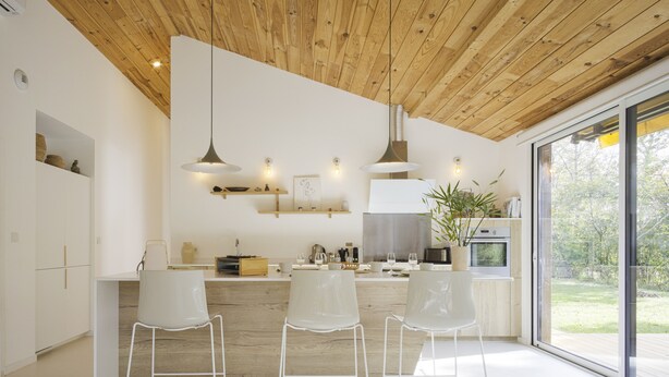 Une cuisine moderne avec des meubles blancs, un plafond en bois et une grande fenêtre offrant une vue sur l’extérieur.