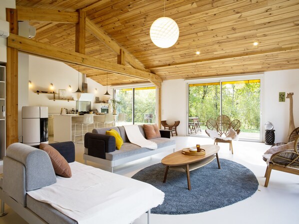 A modern living room with a wooden ceiling, a sofa set, a coffee table, and a dining area with chairs.