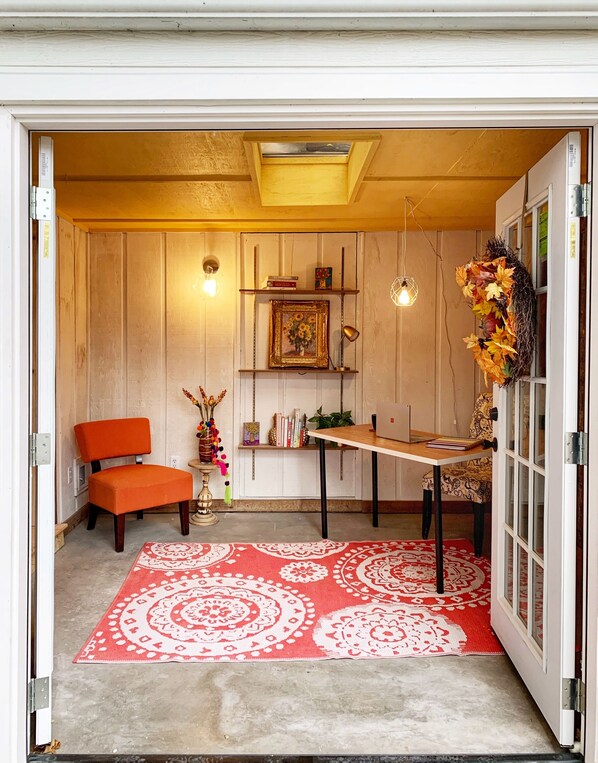 Una stanza accogliente con parete in legno, un tappeto rosso decorato, un tavolo in legno, una sedia ed scaffali con libri e un quadro incorniciato.